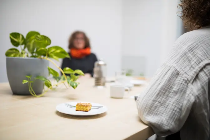 Ein Kuchen auf einem Teller. Im Hintergrund sitzt Maria Steger.